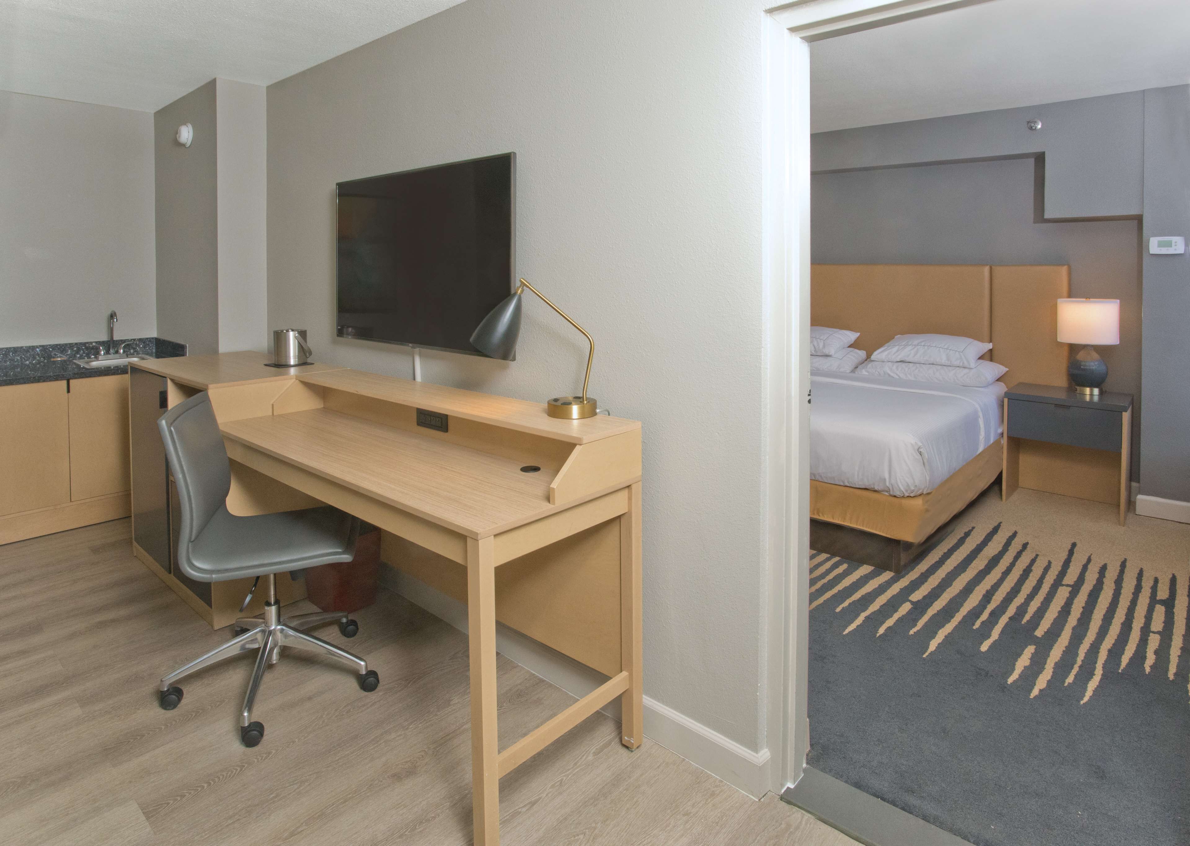 Une chambre d’hôtel avec un bureau en bois, une chaise, une télévision, un lit et une table de chevet avec une lampe.