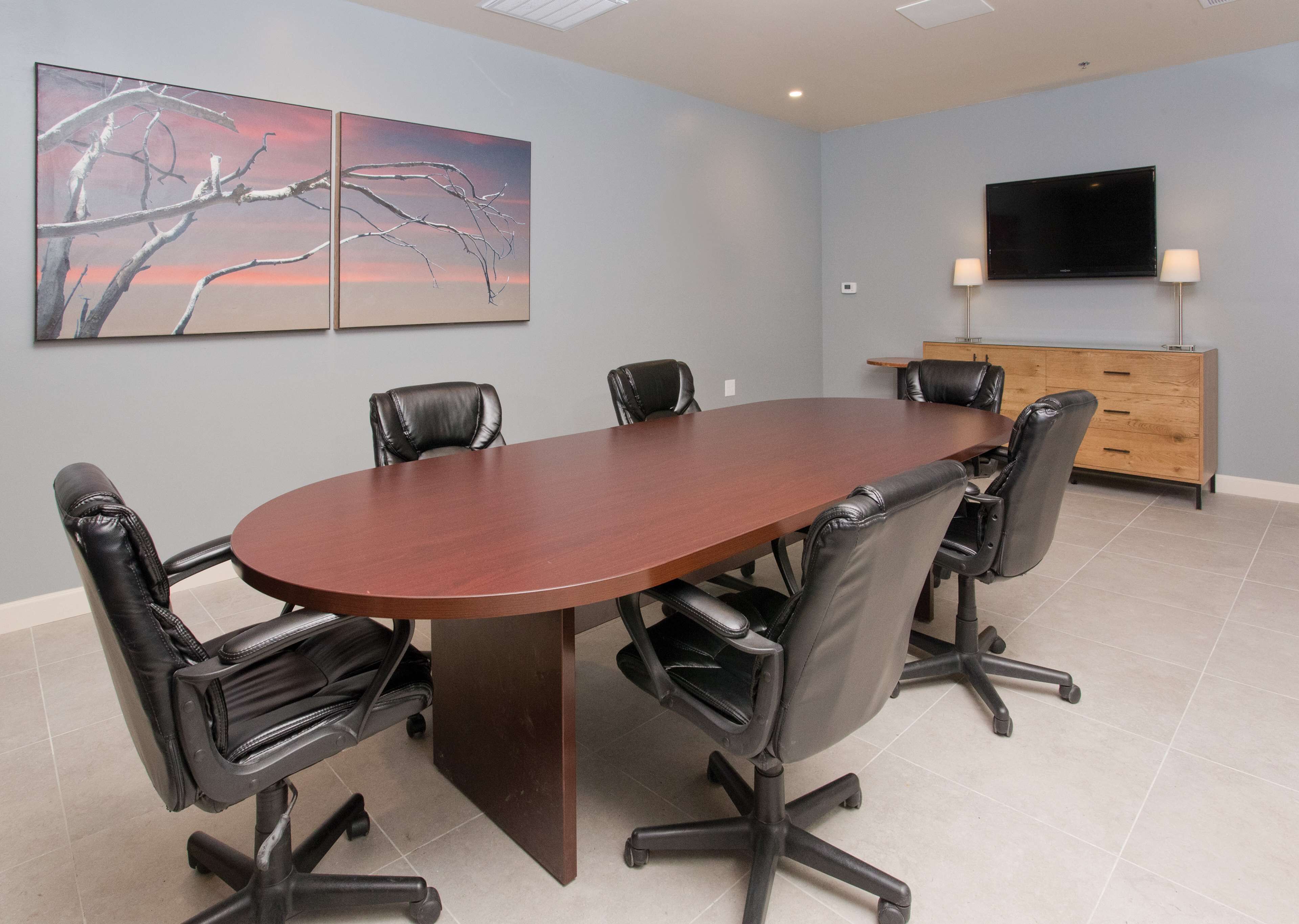 Une salle de conférence dotée d’une grande table ovale, de six fauteuils en cuir noir, d’un meuble en bois et d’un téléviseur à écran plat fixé au mur.