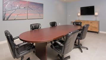 A conference room with a large oval table, six black leather chairs, a wooden cabinet, and a flat-screen TV on the wall.