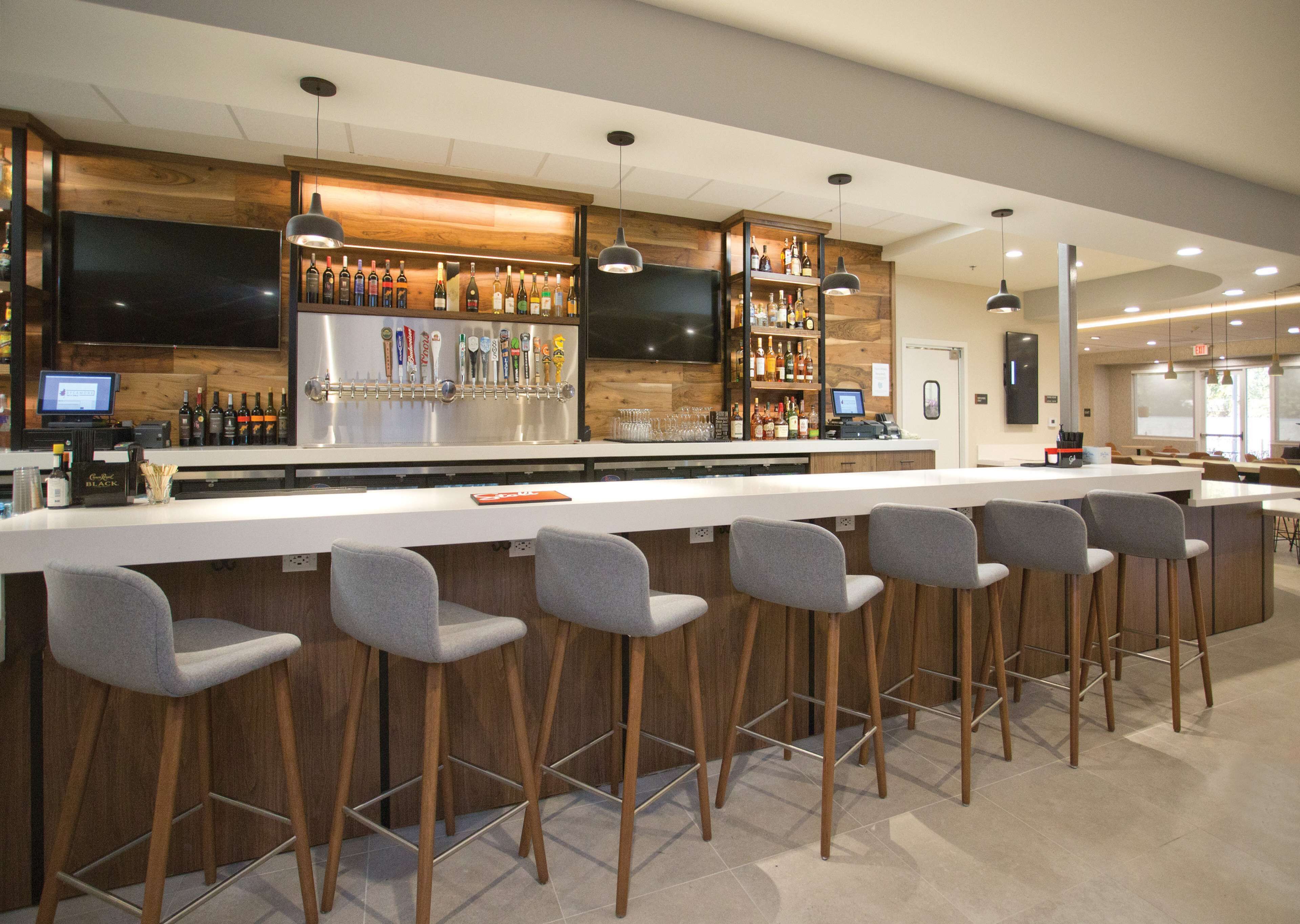 A modern bar area with a long counter, multiple stools, and a variety of bottles and glasses.