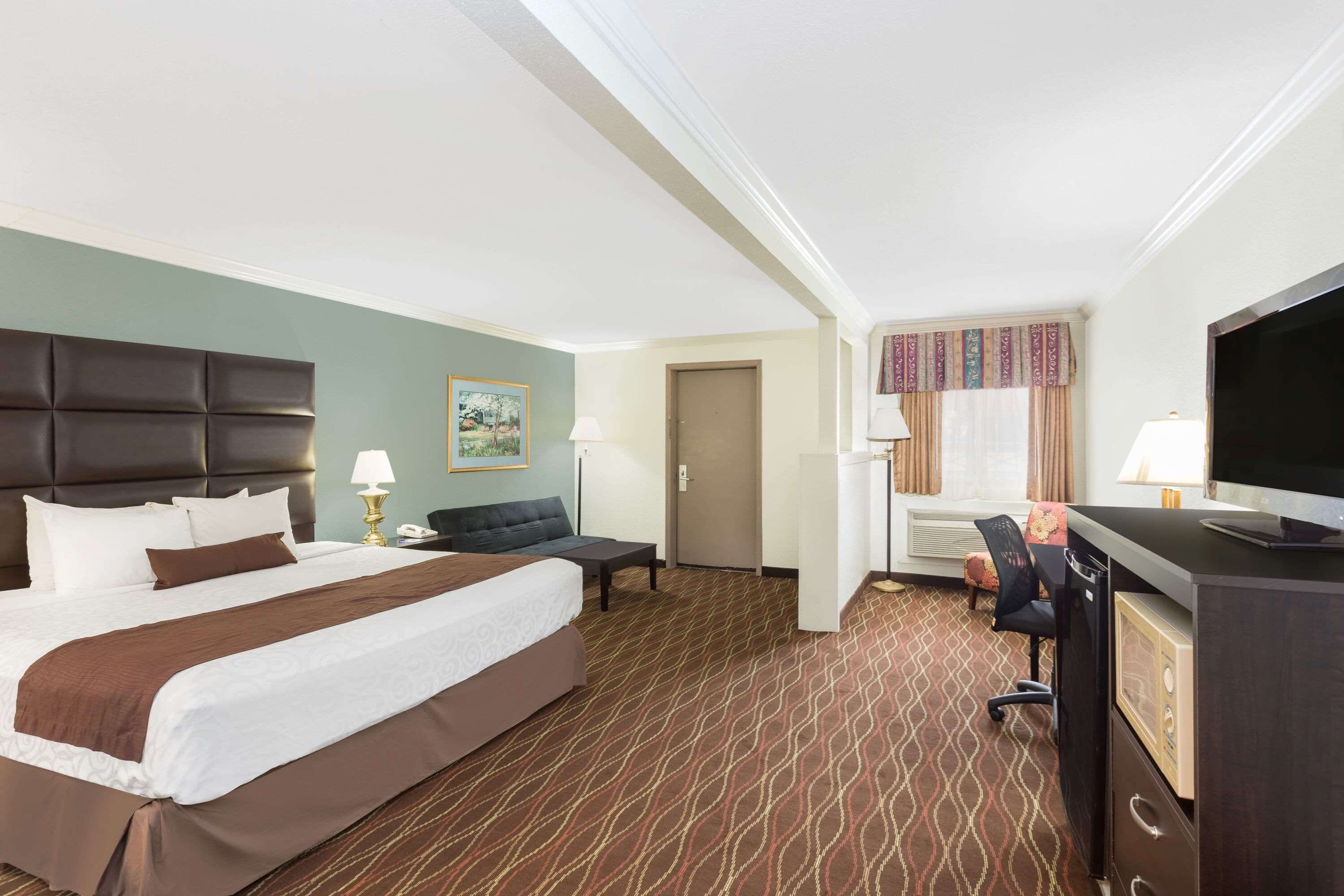 A hotel room with a large bed, a desk with a computer, a chair, a TV, and a door.