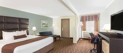 Una habitación de hotel con una cama grande, un escritorio con una computadora, una silla, un televisor y una puerta.