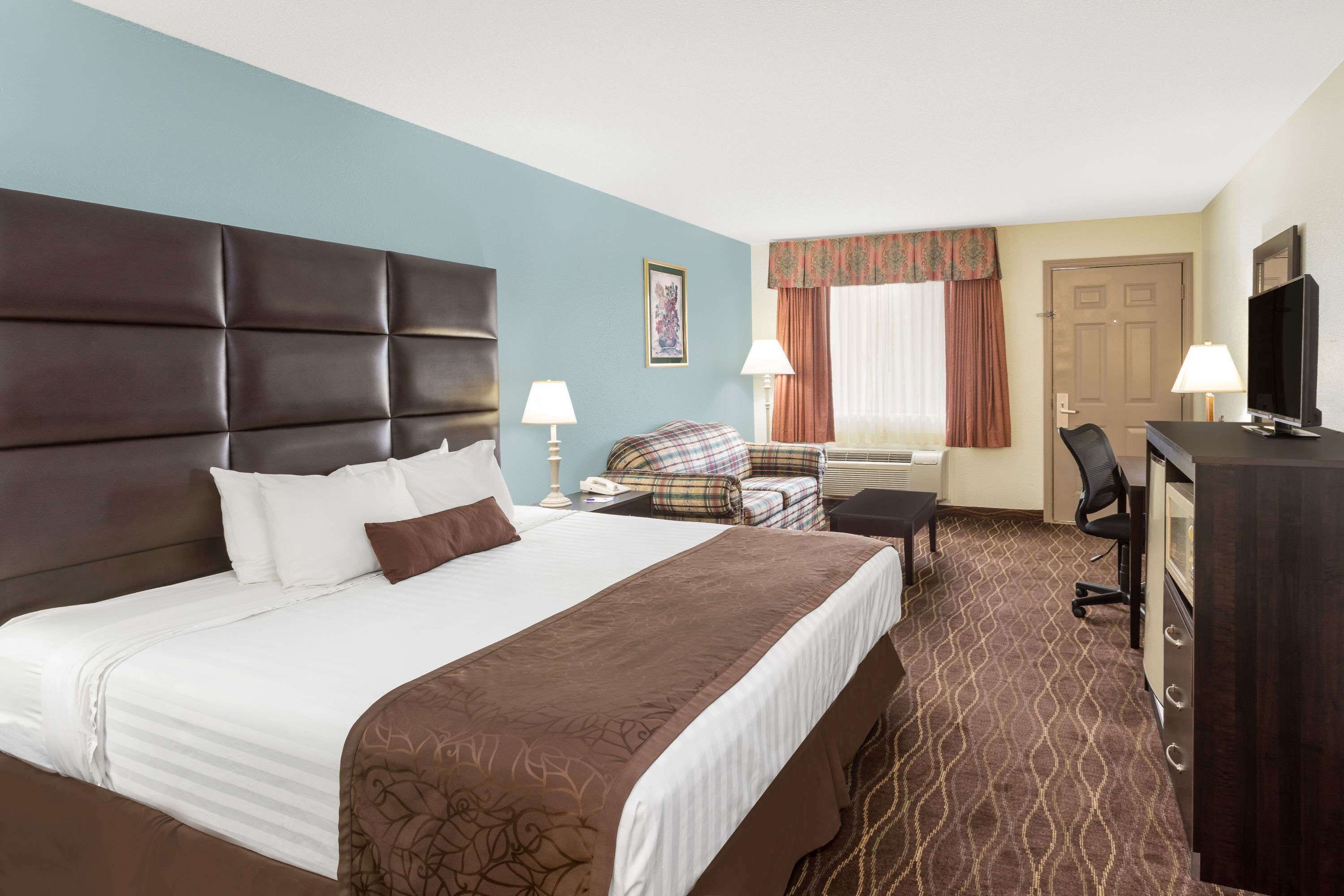 A hotel room with a large bed, a desk, a chair, a television, and a window with curtains.