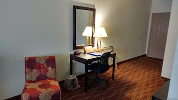 A hotel room with a desk, chair, and a floral-patterned armchair.