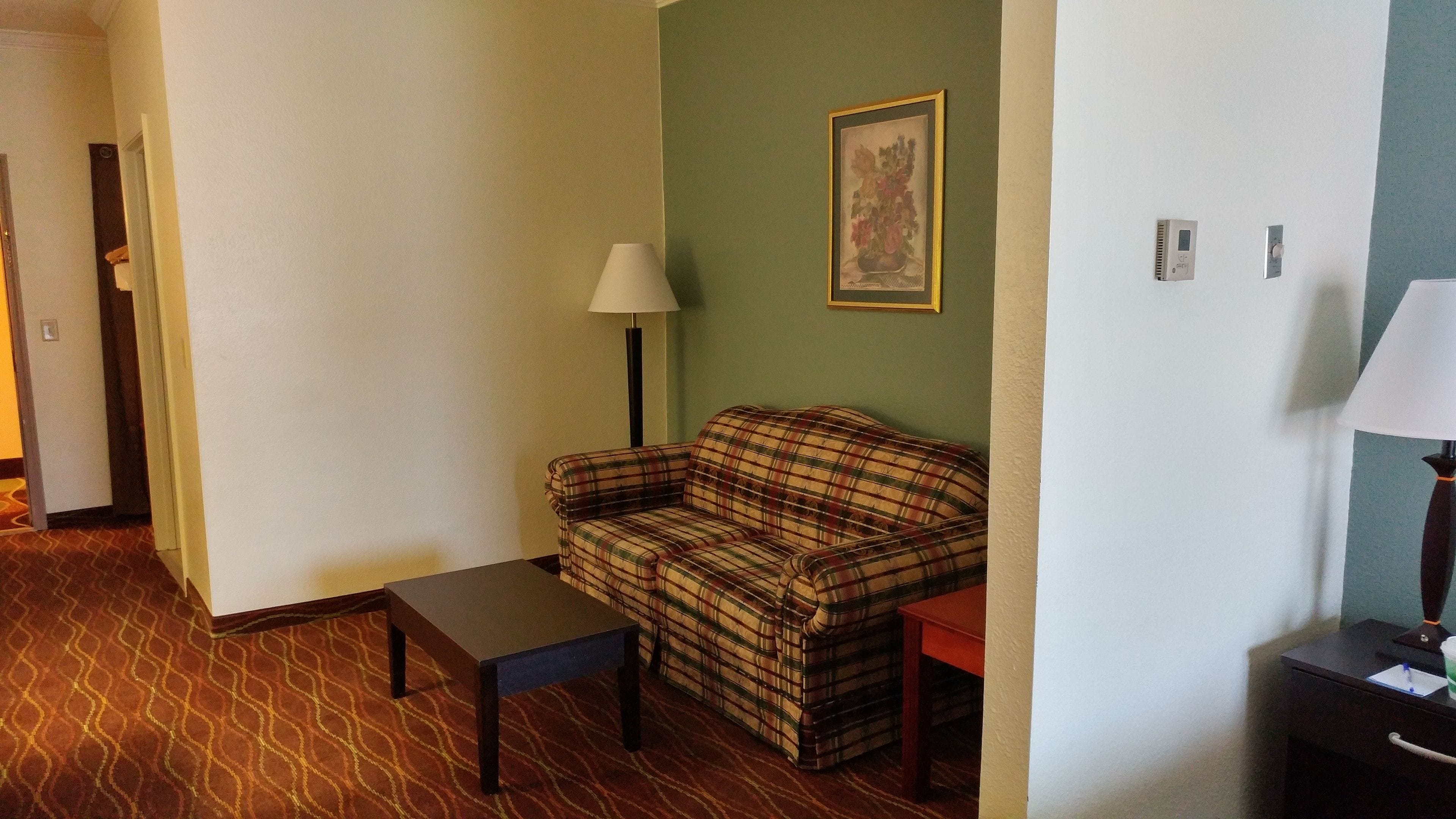 A room with a plaid sofa, a small table, a lamp, and a framed picture on the wall.