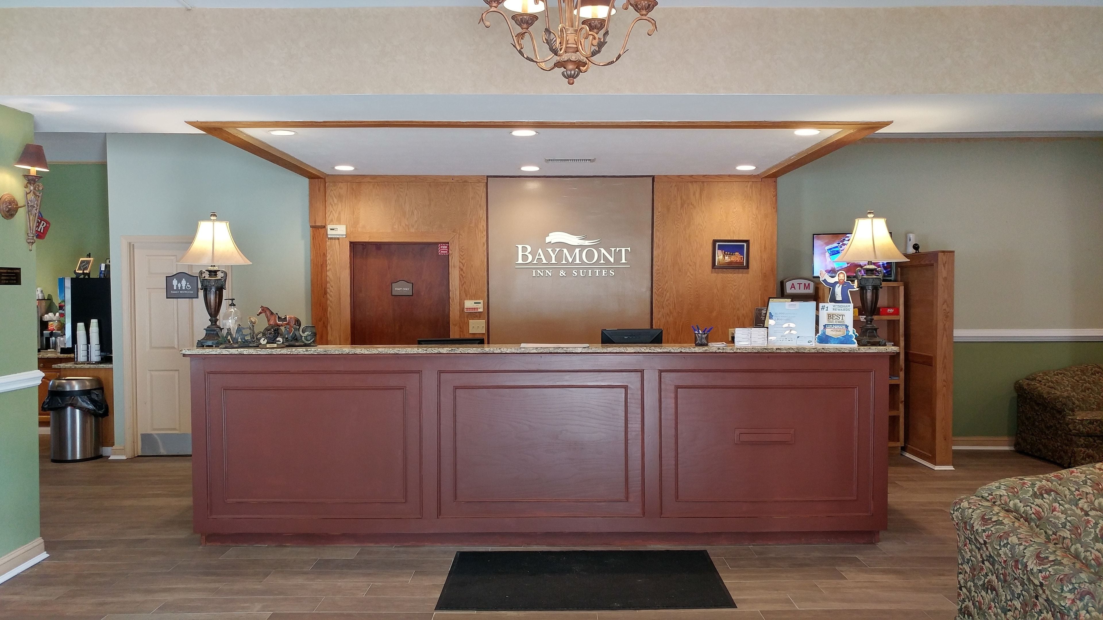 A reception desk at Baymont Inn & Suites with a wooden finish, a chandelier, and a sign indicating family restrooms.