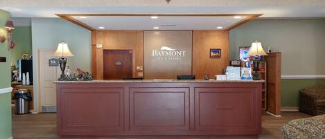 A reception desk at Baymont Inn & Suites with a wooden finish, a chandelier, and a sign indicating family restrooms.