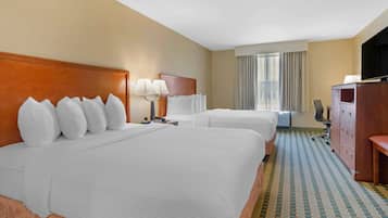 A hotel room with two beds, a desk, a television, and a window with curtains.