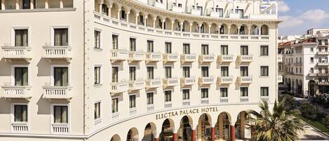 Un hotel grande de varios pisos con fachada clásica, que cuenta con numerosos balcones y un patio central con palmeras.
