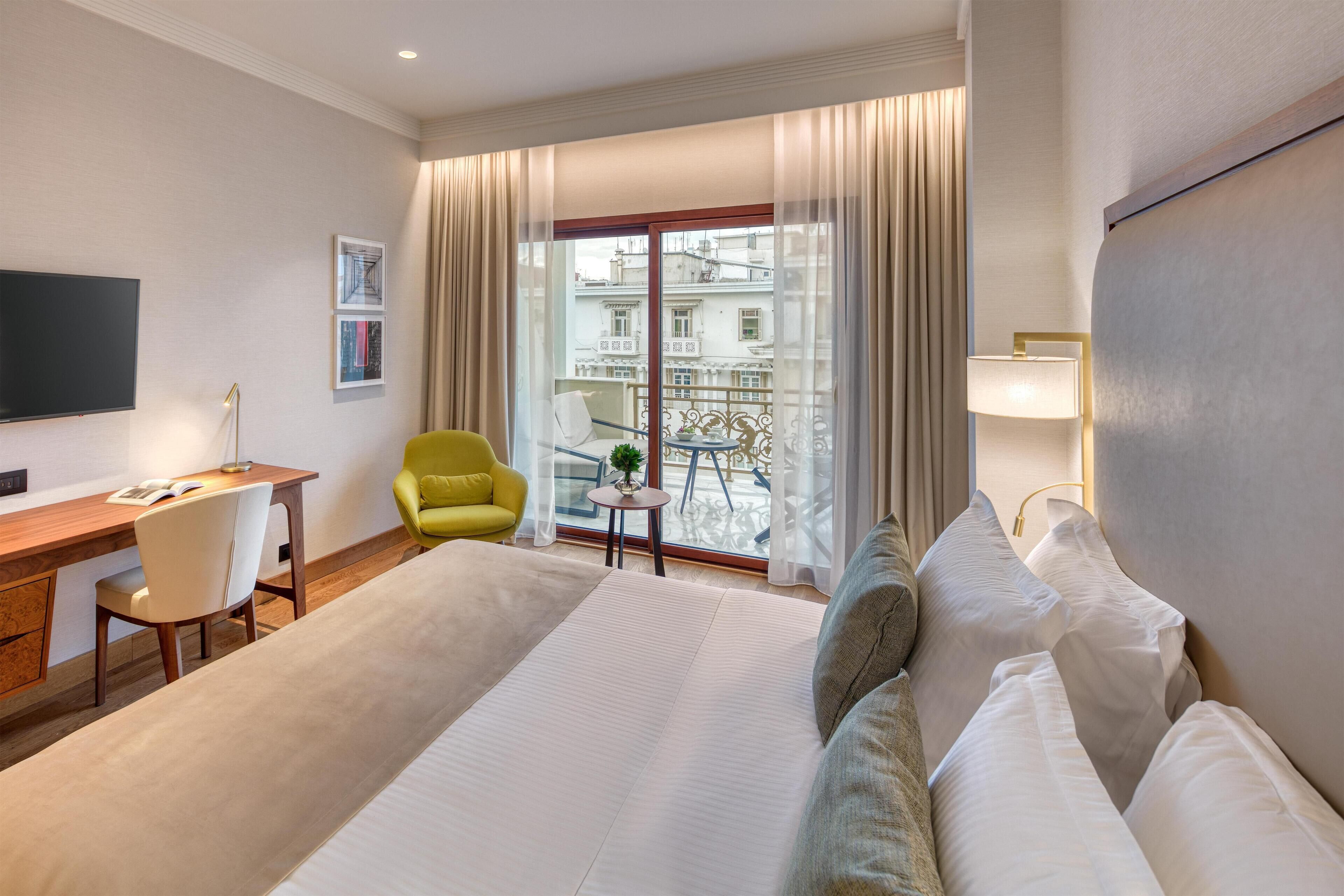 Une chambre d’hôtel avec un grand lit, un bureau avec une chaise, une petite table avec une lampe et un téléviseur.