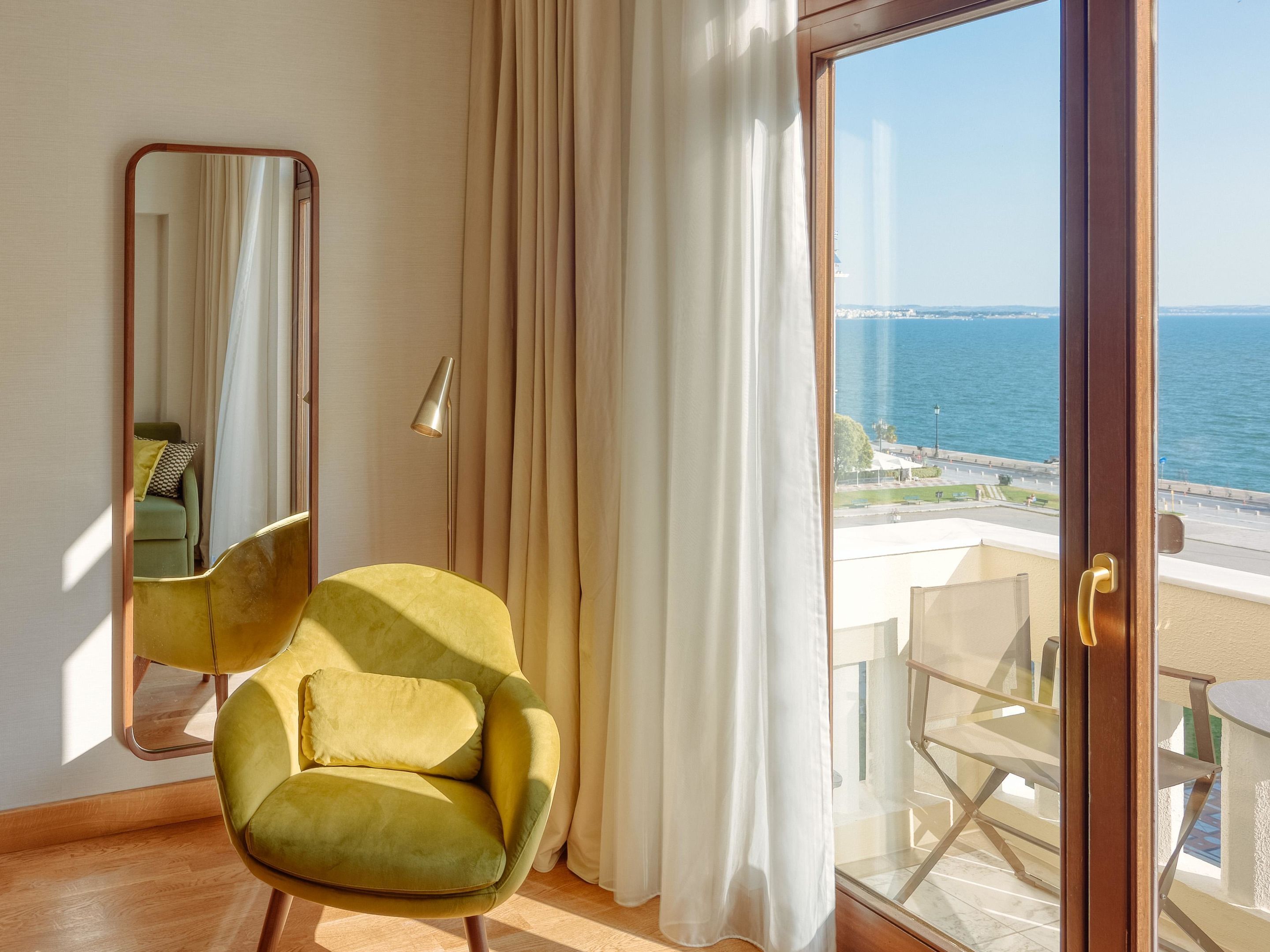 A room with a view of the sea, a green armchair, a large mirror, and a sliding glass door.