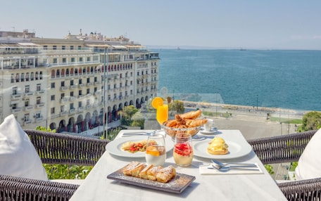 A table with breakfast items and a glass of orange juice, overlooking a coastal cityscape.