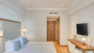 A hotel room with a bed, desk, chair, TV, and a door leading to another room.