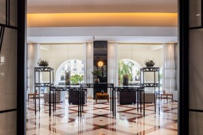 Un hall d’entrée spacieux doté d’un sol aux motifs géométriques, un espace de détente central avec deux canapés et une table, et de grandes fenêtres offrant une vue sur le paysage urbain.