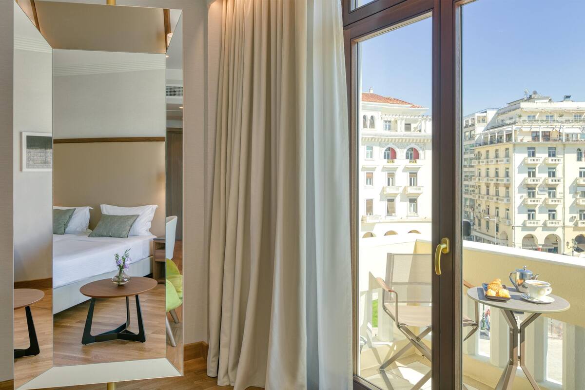 Une chambre d’hôtel avec un lit, une petite table sur laquelle est posé un vase, et un balcon avec une table et des chaises.