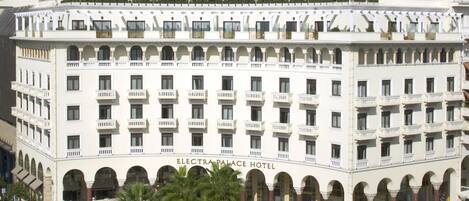 A multi-story hotel with a central courtyard, arched balconies, and a sign reading "Electra Palace Hotel".