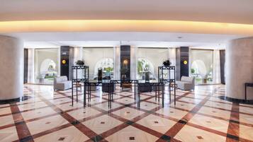 A spacious lobby with a checkered floor, a central table with chairs, and large windows offering views of the outside.