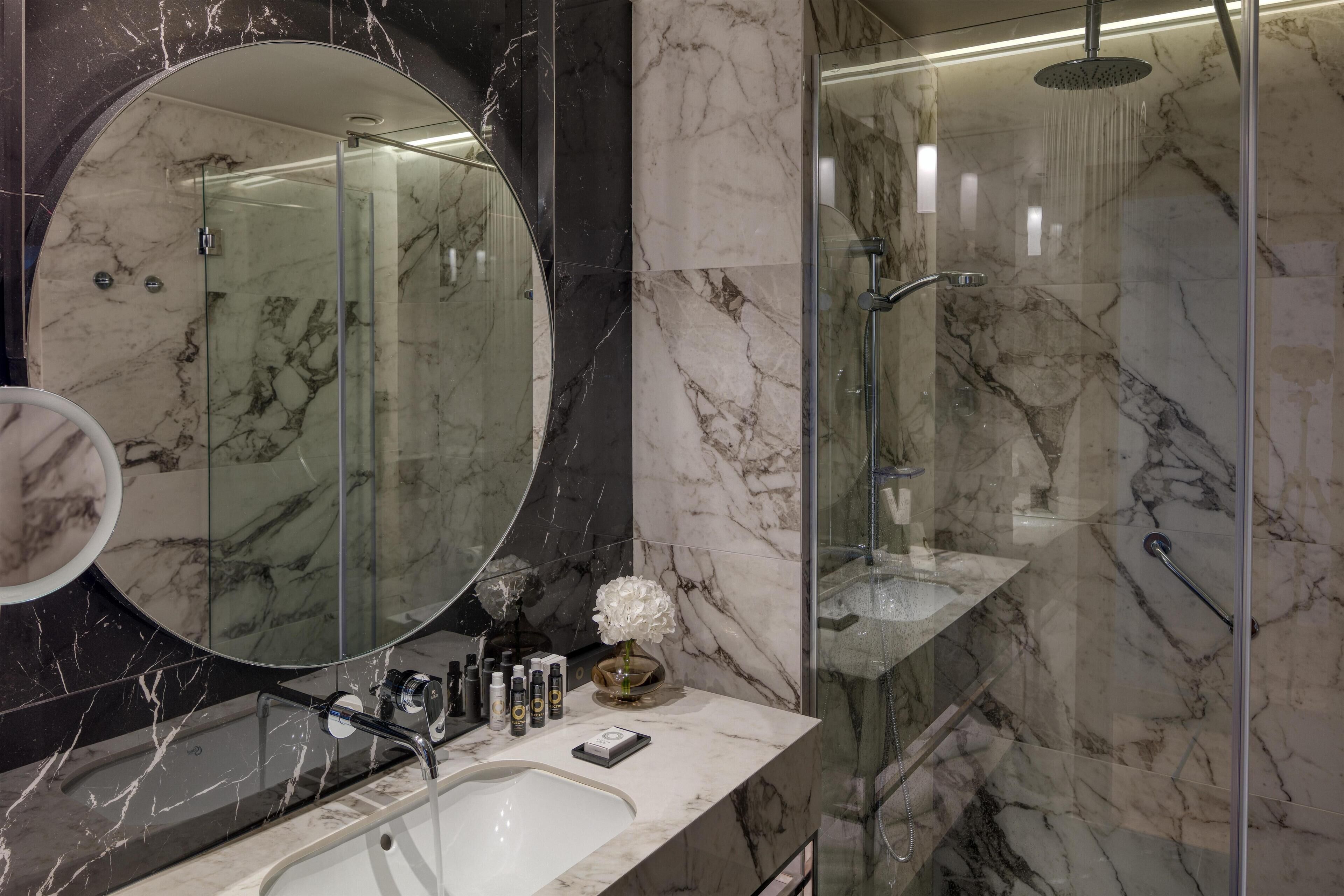 A modern bathroom with a marble sink, a large mirror, and a glass-enclosed shower.