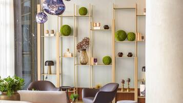 Uma sala de estar moderna com sofá, poltrona e mesa de centro, uma estante com objetos decorativos e uma janela grande.