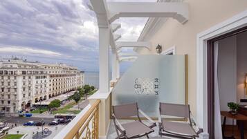 A balcony with two chairs, a view of a large hotel, and a street with cars and pedestrians.