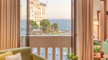 A room with a view of a waterfront, a sofa, a small table with a plant, and a chair.