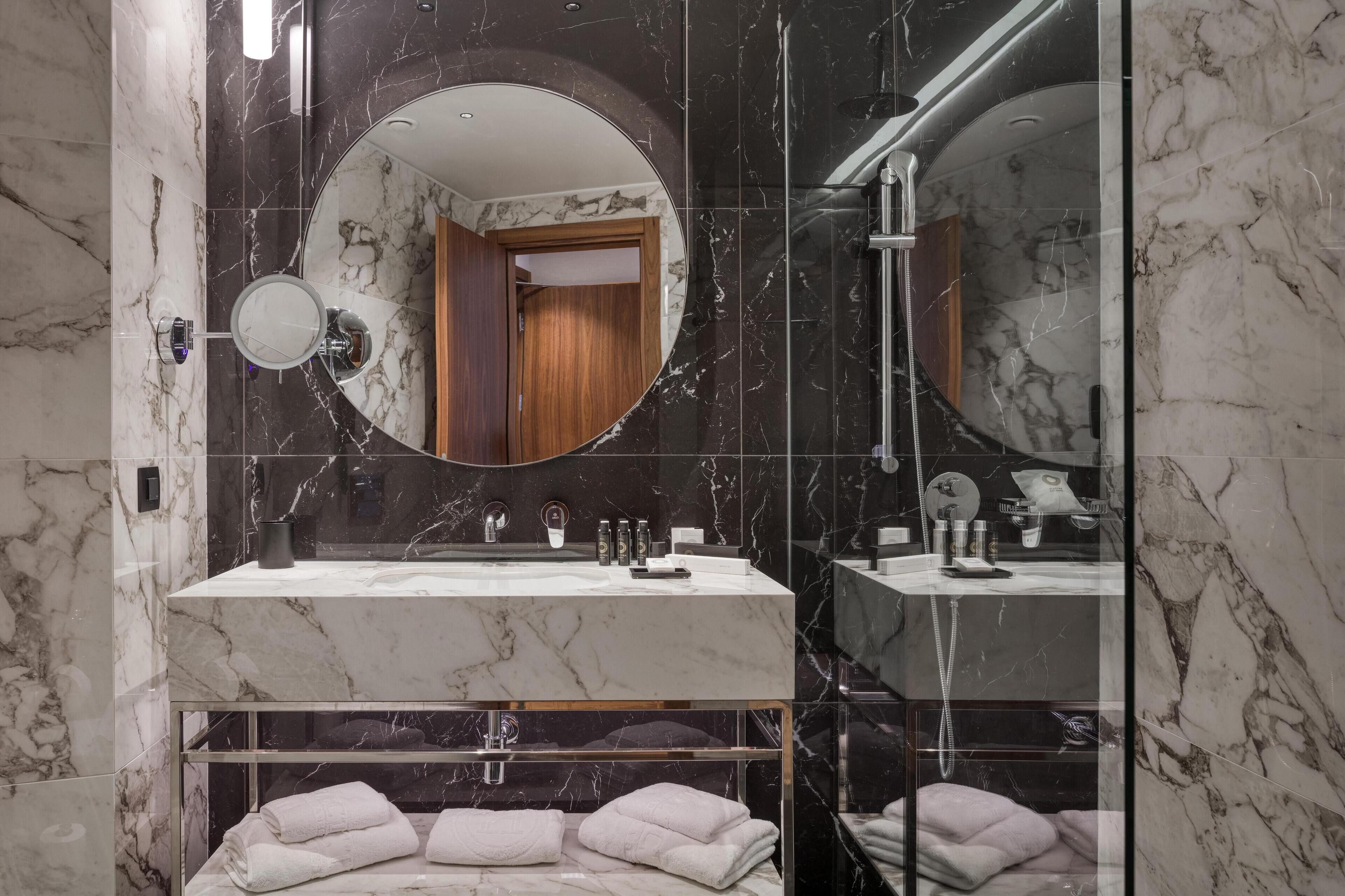 A modern bathroom with a marble vanity, a round mirror, and a shower area.