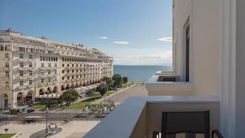 A view from a balcony overlooking a large building with multiple floors and balconies, a clear sky, and a body of water in the distance.