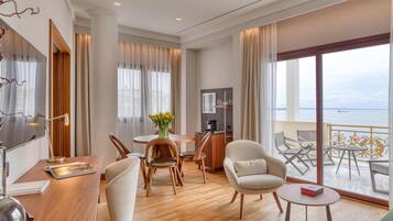 Habitación de hotel moderna con comedor, sofá, televisor y balcón con vista al mar.
