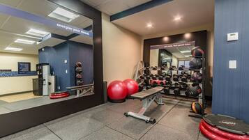 Un gimnasio con equipamiento de ejercicio, incluyendo una banca, balones de ejercicio rojos y una variedad de pesas.