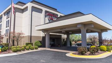Un Hampton Inn con entrada despejada, estacionamiento y asta de bandera.