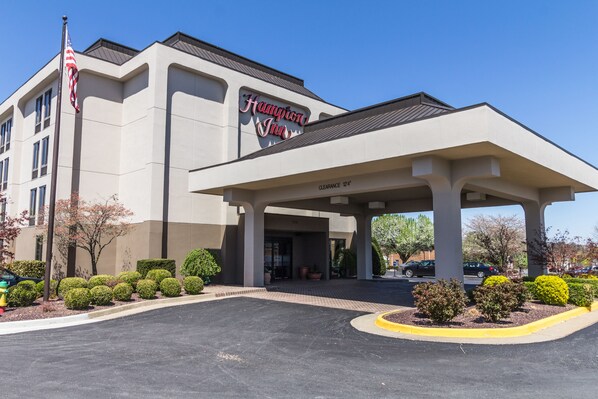 Un Hampton Inn con entrada despejada, estacionamiento y asta de bandera.