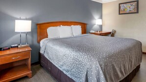 A hotel room with a bed, two bedside tables, a lamp, a nightstand, and a wall map.