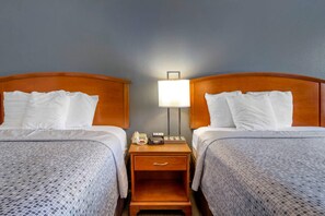 A hotel room with two beds, a nightstand with a lamp, a phone, and a small table.
