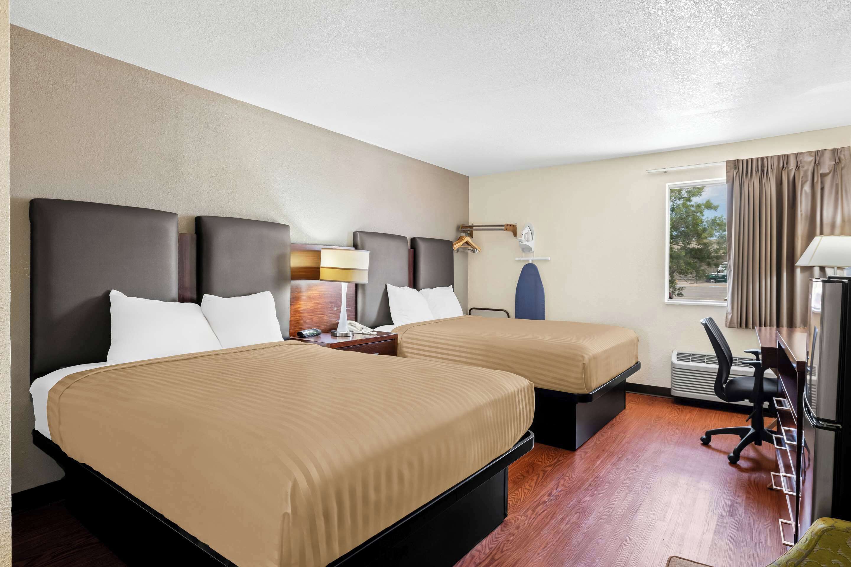 A hotel room with two beds, a desk, a chair, a lamp, and a window with curtains.
