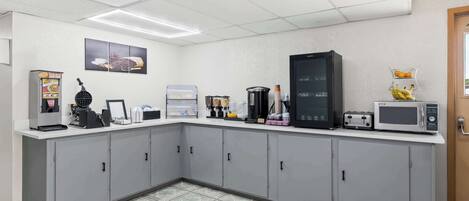 A kitchen with grey cabinets, a coffee machine, a microwave, and a refrigerator.
