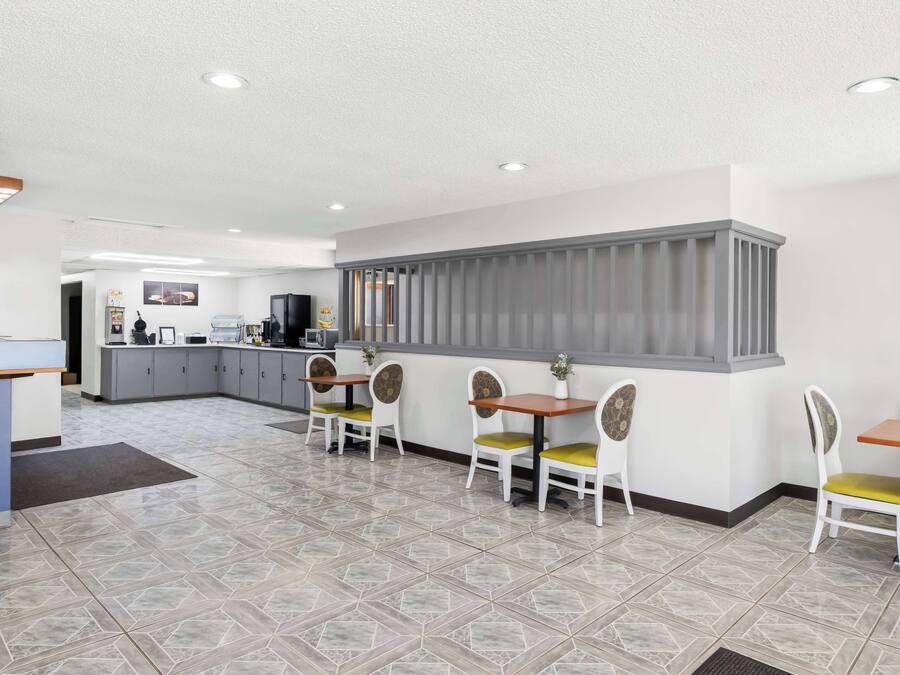 A modern restaurant with a central counter, multiple tables with chairs, and a tiled floor.