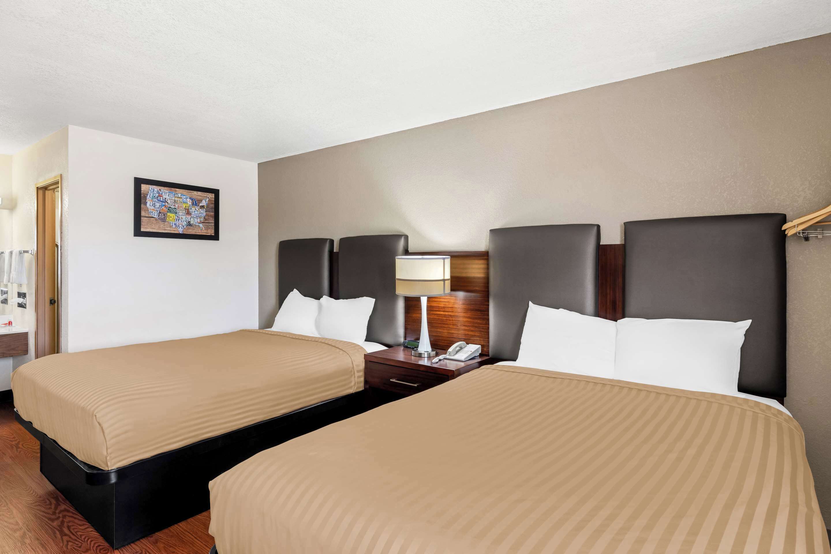 Una habitación de hotel con dos camas, una mesita de noche con lámpara y un cuadro enmarcado en la pared.