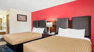 A hotel room with two beds, a red accent wall, a framed map, and a nightstand with a lamp and phone.