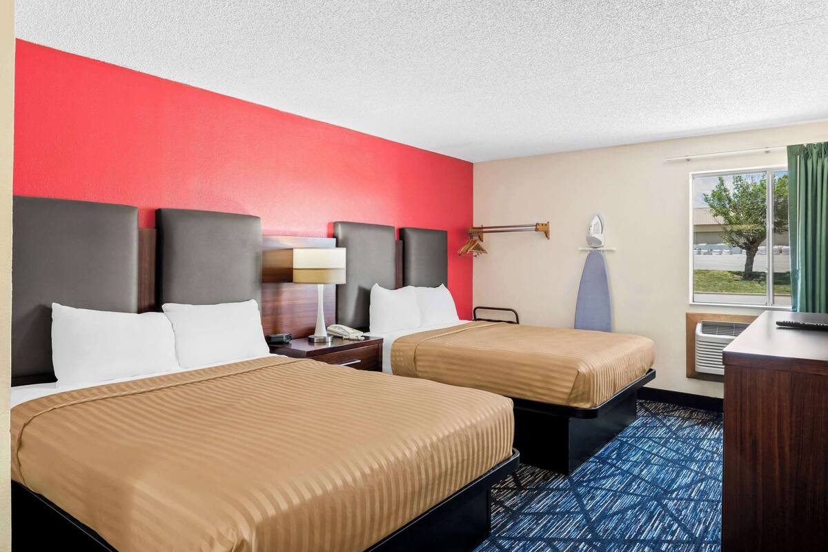 A hotel room with two beds, a desk, a lamp, and a window with curtains.