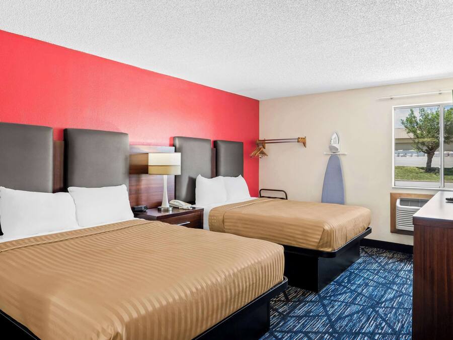 Habitación de hotel con dos camas, un escritorio, una lámpara y una ventana con cortinas.