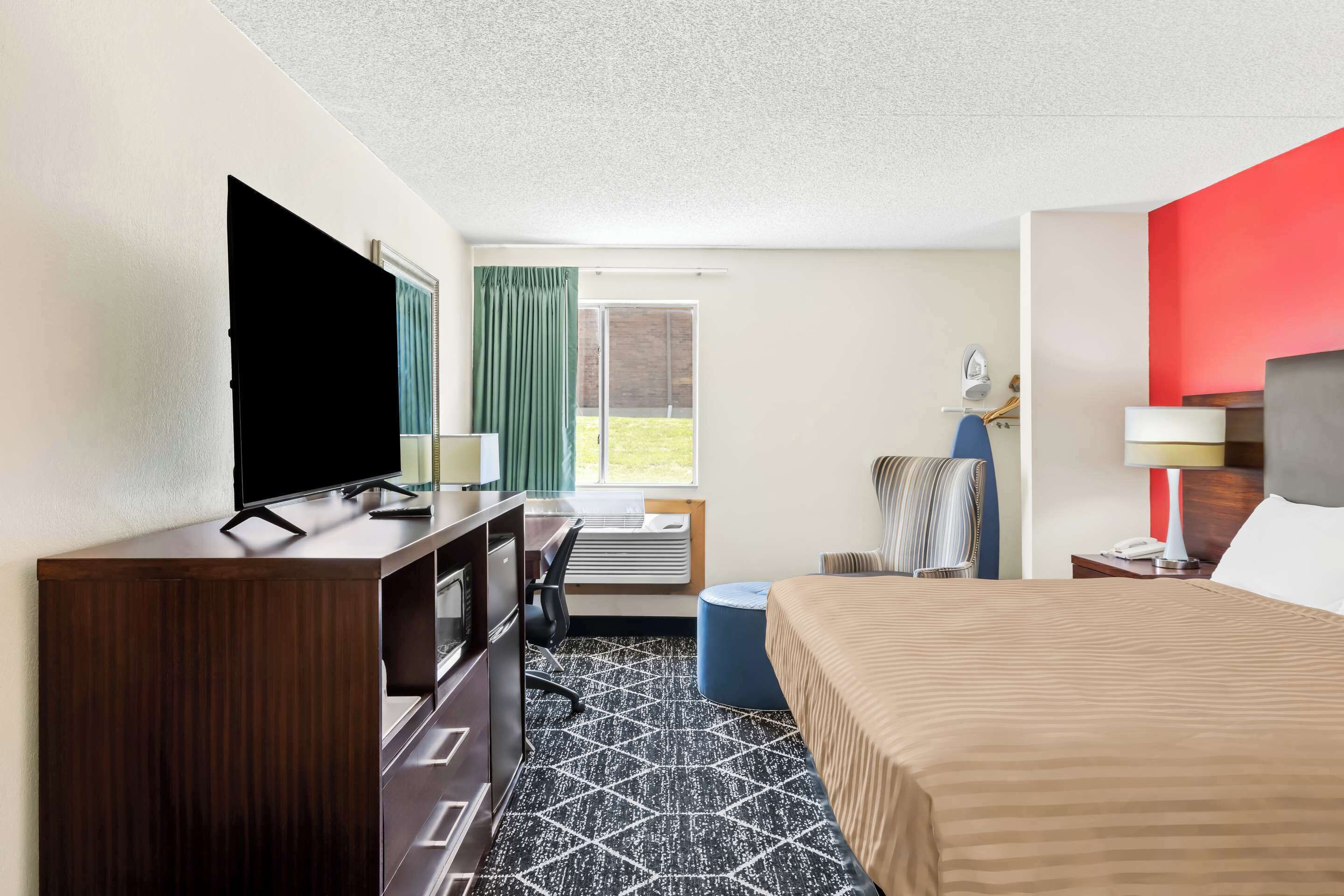 Une chambre d’hôtel comprenant un lit, un bureau avec un ordinateur, une télévision, une fenêtre avec des rideaux et une vue sur l’extérieur.