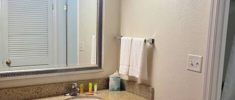 A bathroom with a granite countertop, wooden cabinets, a white sink, a large mirror with a decorative frame, and a towel hanging on a rack.