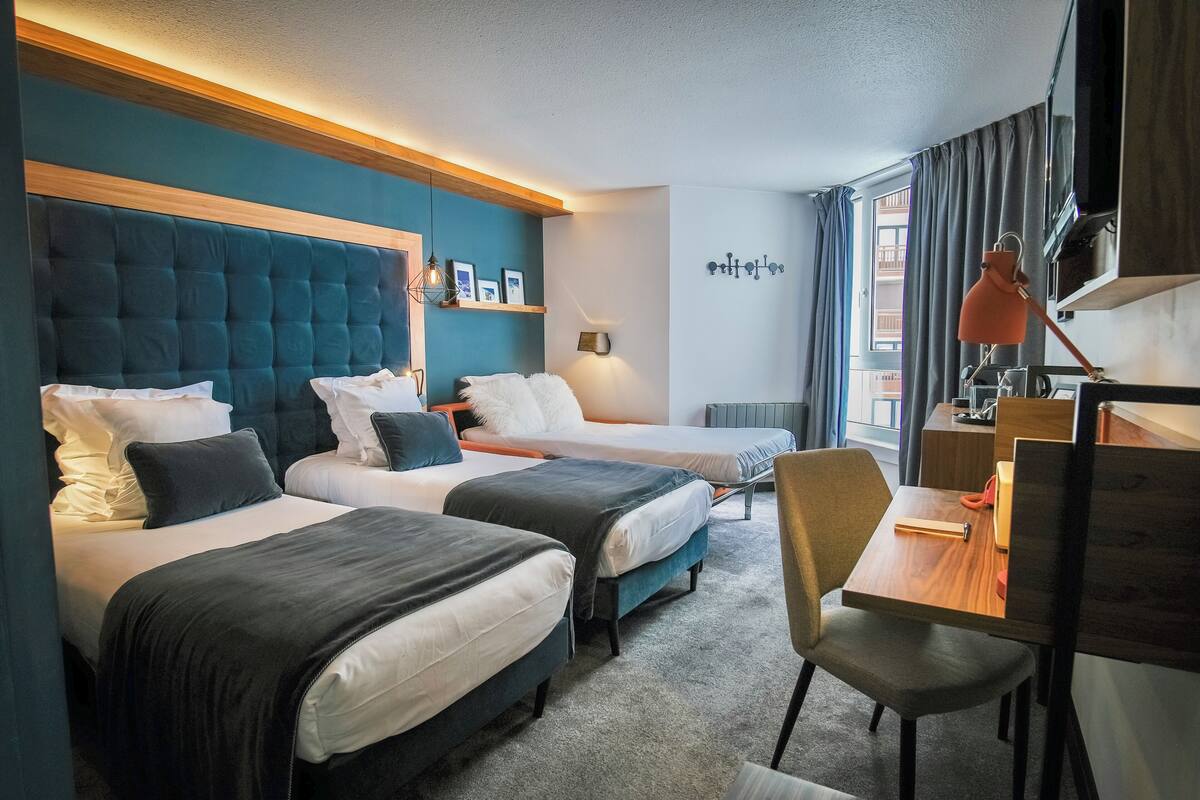 Ein Hotelzimmer mit zwei Betten, einem Schreibtisch, einem Stuhl, einem Fernseher und einem Fenster mit Vorhängen.