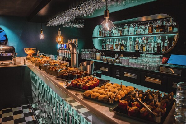 A bar area with a variety of food items, a bar counter, and shelves of liquor bottles. - Hôtel Fahrenheit Seven Val Thorens (Les Belleville)