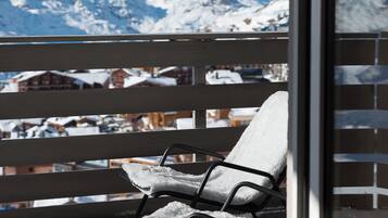 A balcony with a view of snow-covered mountains, a chair, and a glass door.