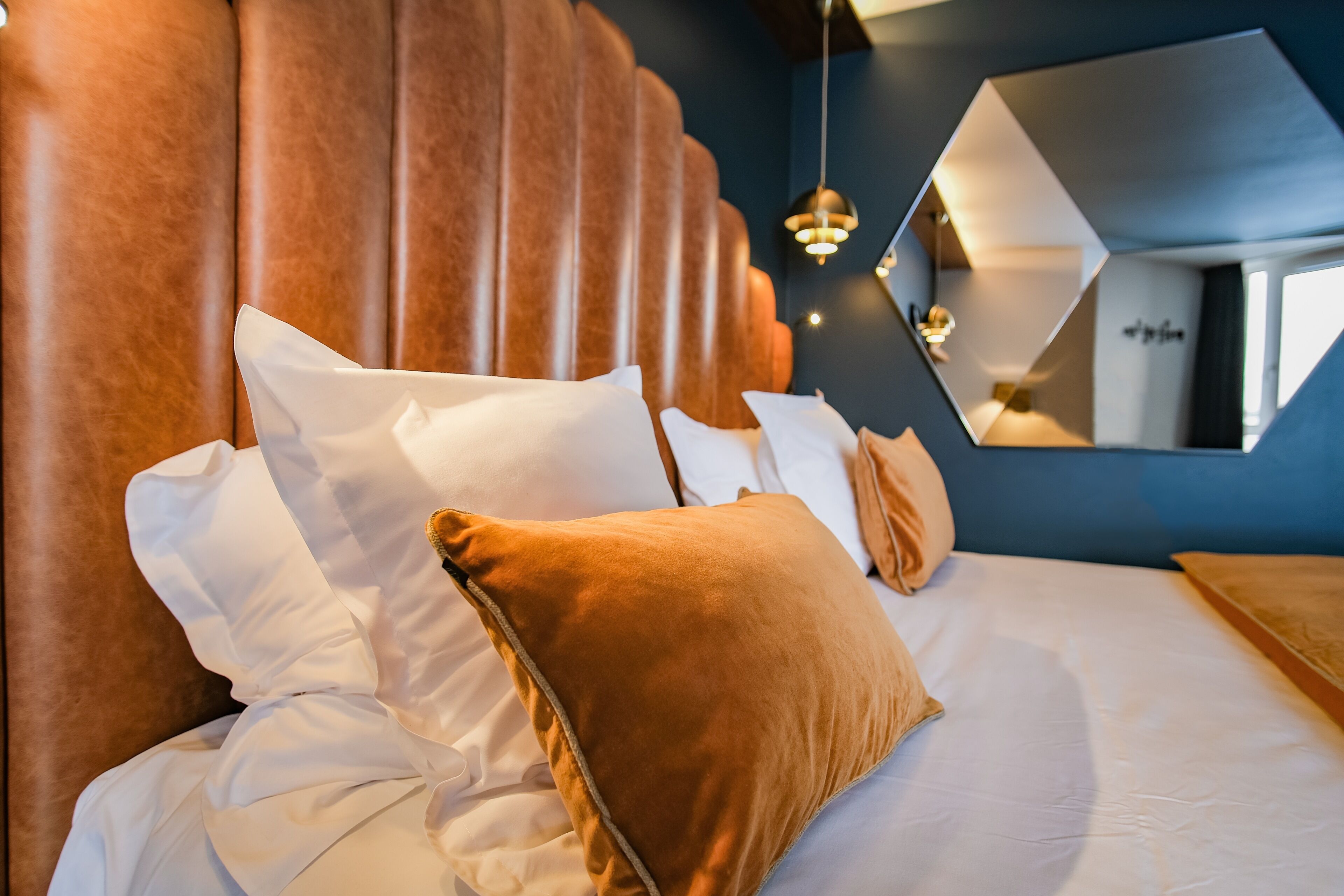 A hotel room with a large bed, a headboard, a mirror, and a hanging light fixture.