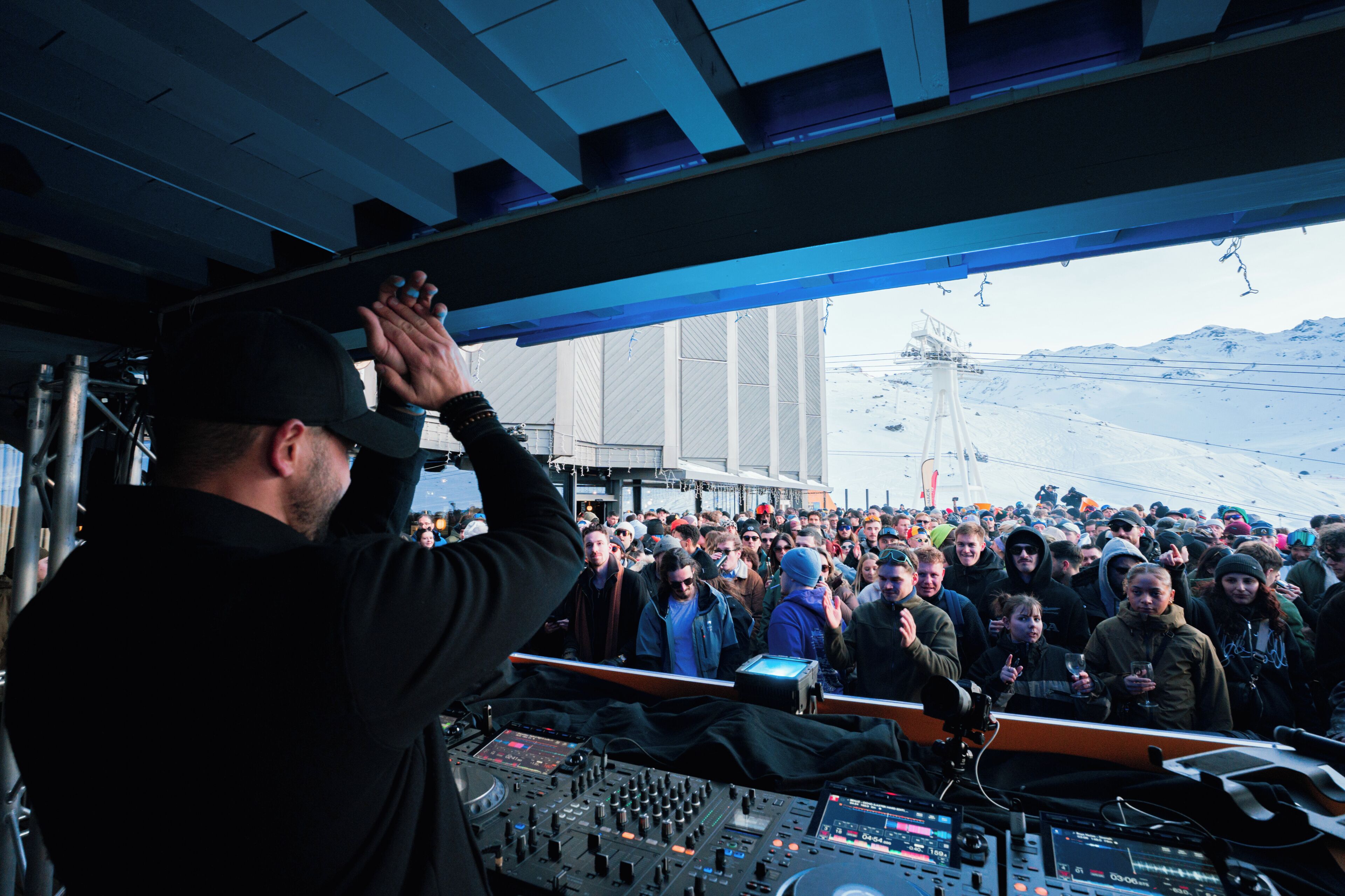 Une cabine de DJ avec des panneaux de contrôle et une foule de personnes à l’extérieur.