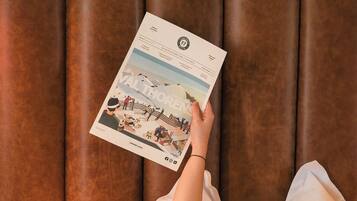 A person lying in bed with a magazine, a brown headboard, and white bedding.