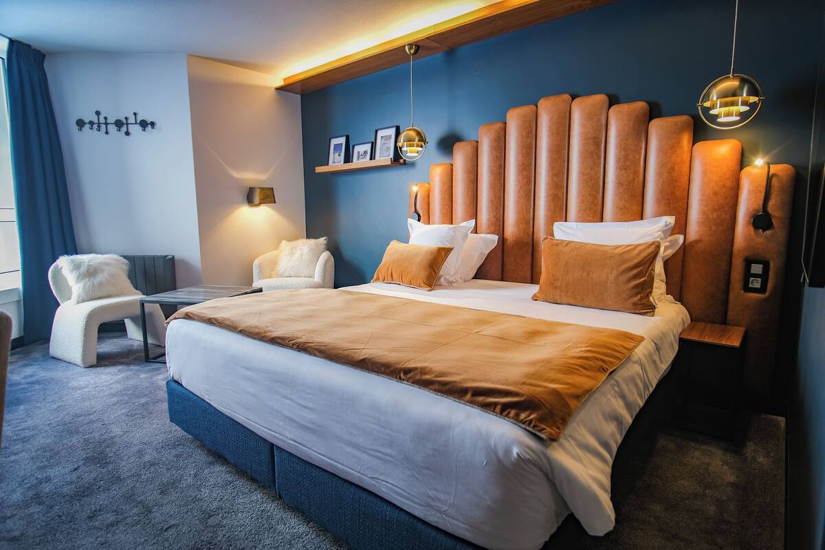 Ein modernes Hotelzimmer mit einem großen Bett, einem Sessel, einem Schreibtisch und einer Wandleuchte.
