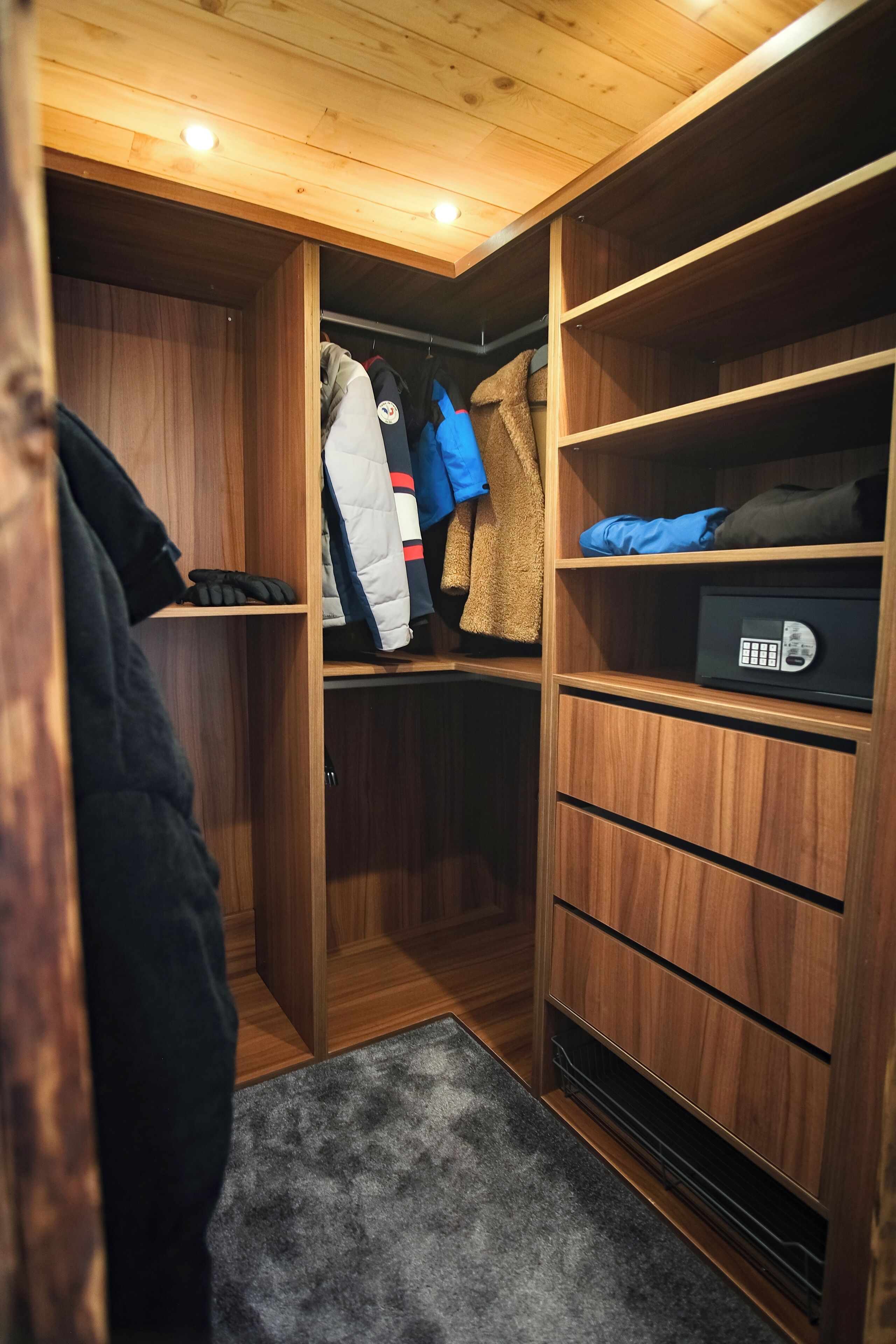 A wooden closet with shelves and drawers, a small rug, and a coat rack with jackets.